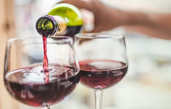 Close-up of red wine pouring from green bottle into clear glass.