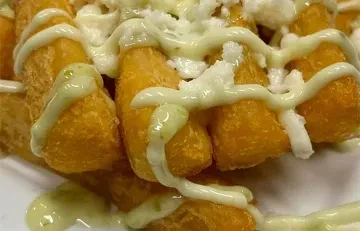 Plate of golden-brown fried food with white and green sauces, white crumbles.