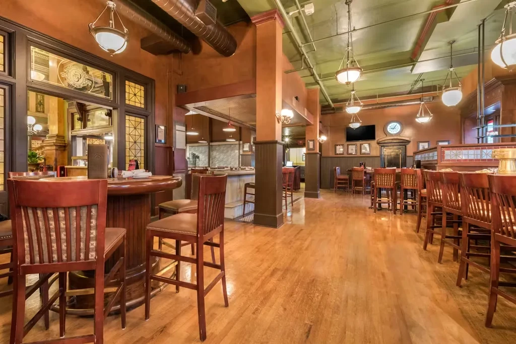 Empty upscale restaurant bar with wooden high-top tables and warm lighting.