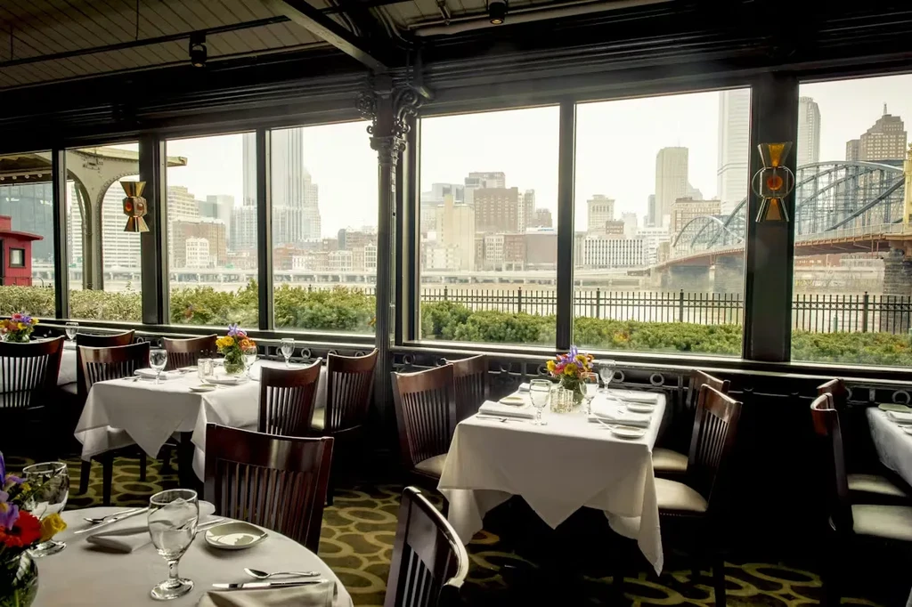 Empty elegant restaurant overlooking a hazy city skyline and bridge.