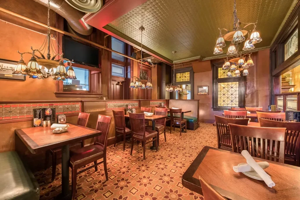 Empty vintage restaurant with ornate wood, green booths, and stained glass.