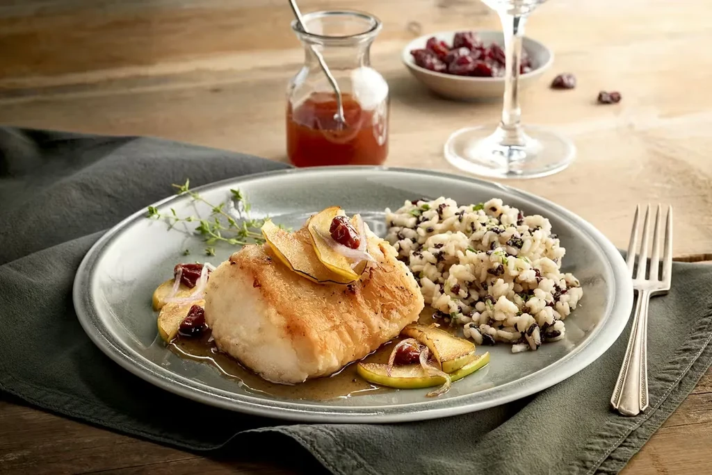 Pan-seared white fish with apple, thyme, and mixed rice on plate.