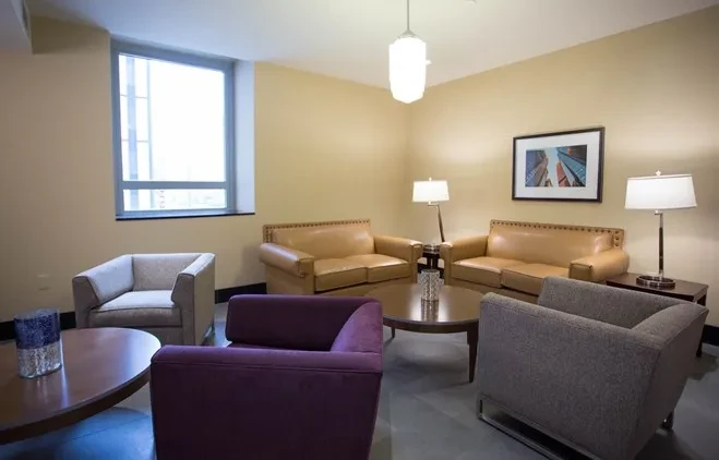 Well-lit, empty lounge with tan sofas, grey armchairs, and coffee tables.