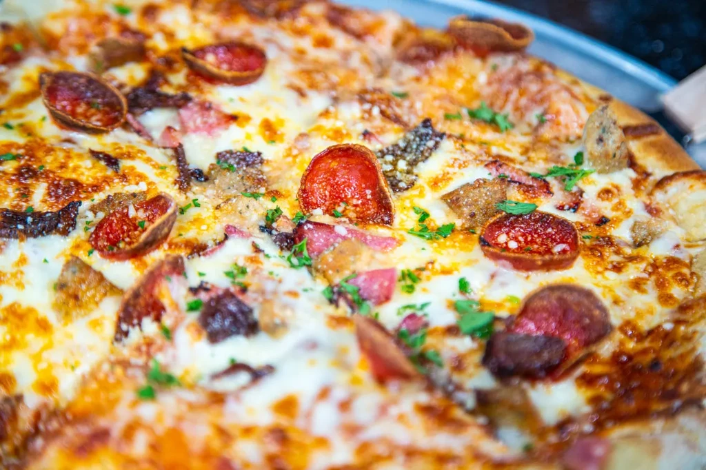 Close-up of a pizza with melted cheese, meat toppings, and herbs.