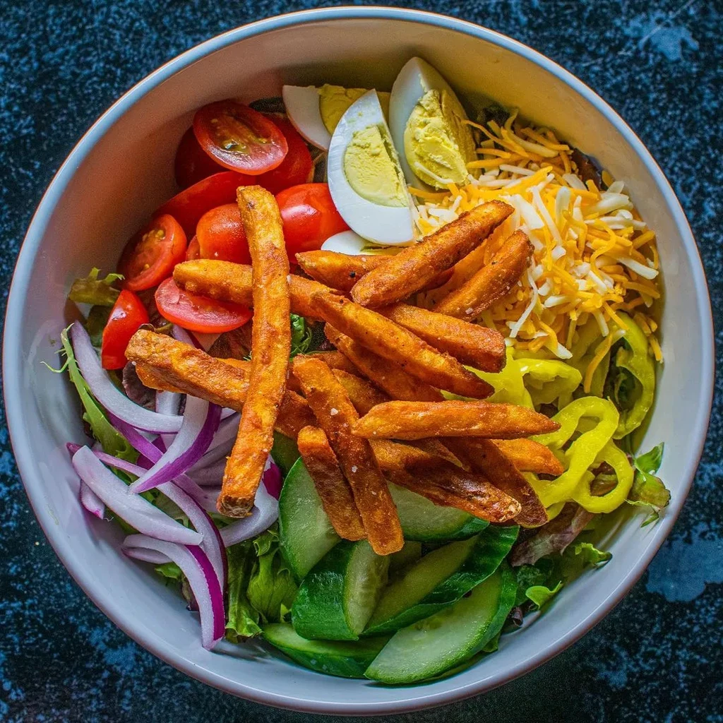 Overhead salad with sweet potato fries, eggs, tomatoes, cheese, and lettuce.