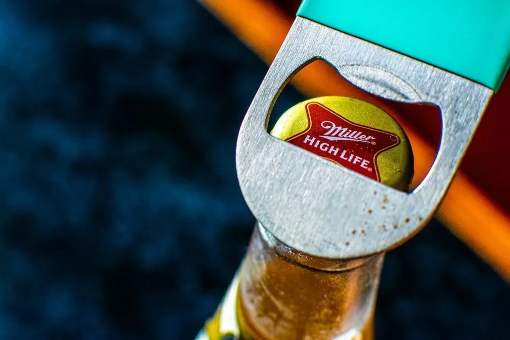 Metallic teal bottle opener removing a Miller High Life bottle cap.