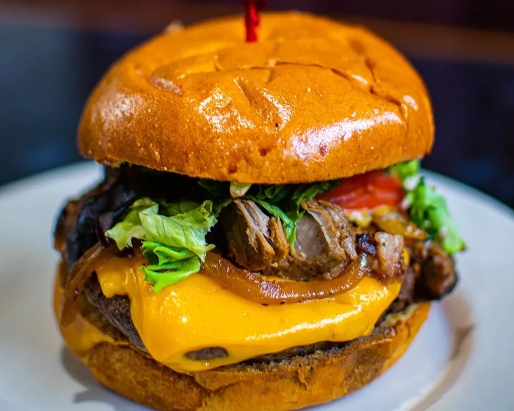 Burger with melted cheese, pulled meat, lettuce, tomato, and onions.