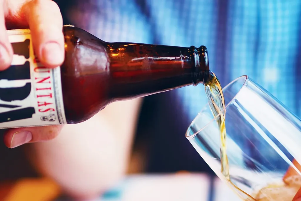 Hand pours golden beer from Lagunitas bottle into clear glass.
