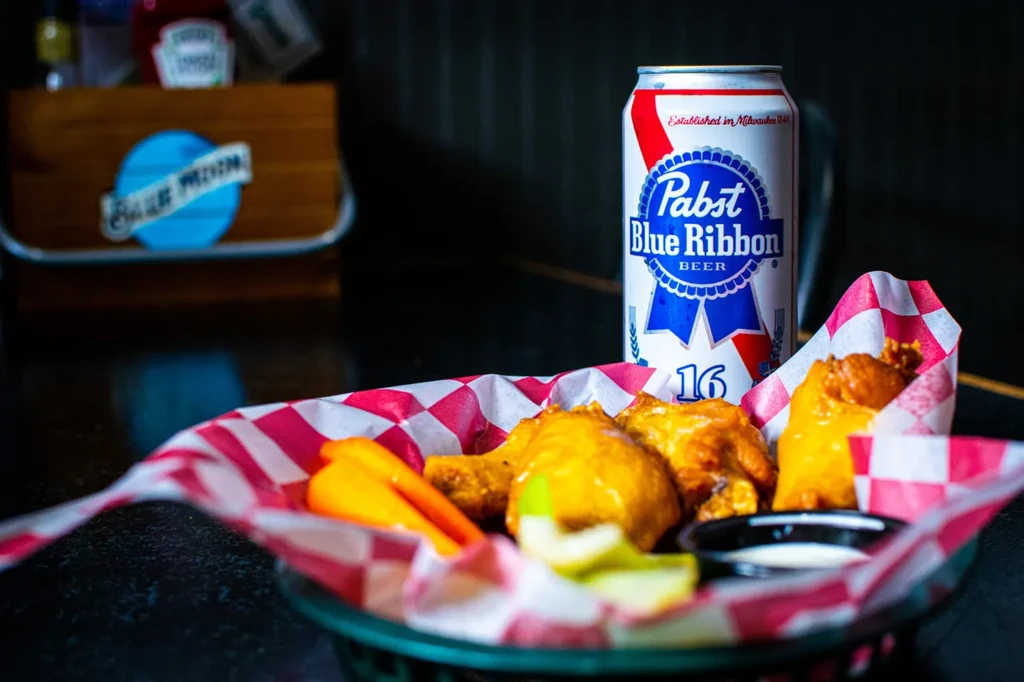 Fried chicken wings, vegetables, dipping sauce, and Pabst Blue Ribbon beer.