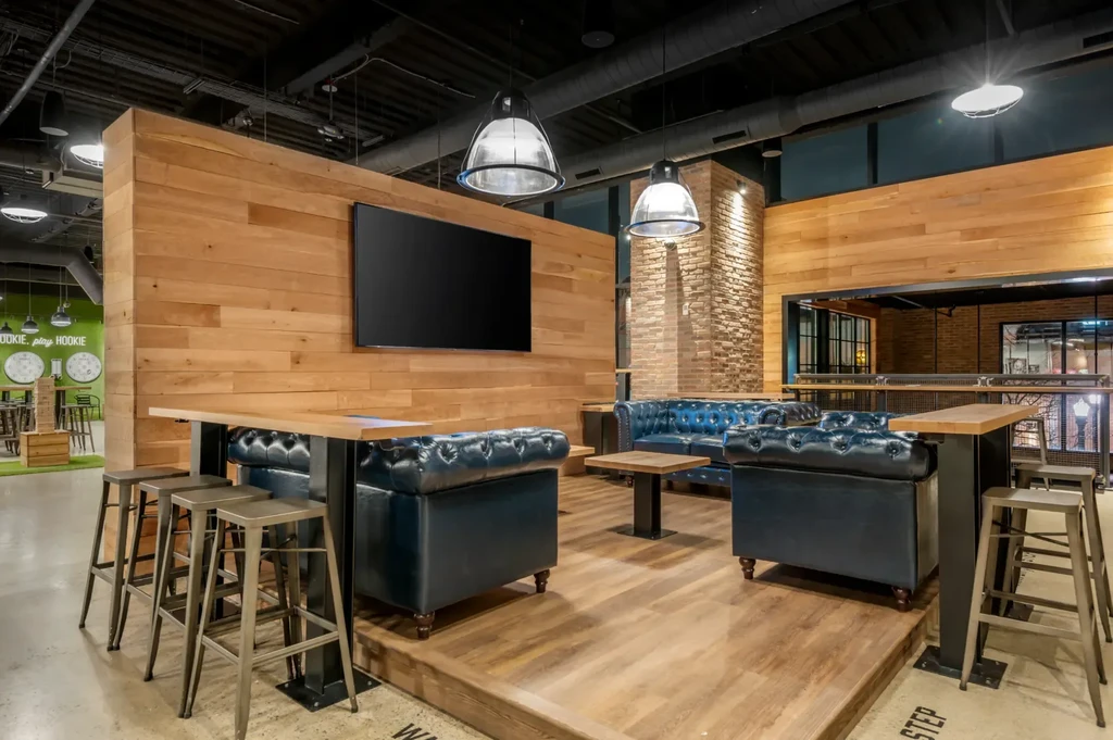 Modern lounge interior with blue tufted sofas, slatted walls, and games.