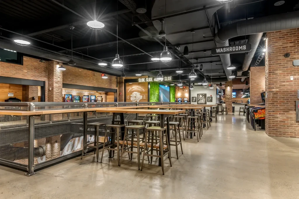 Empty industrial restaurant with high-top tables, moss wall, and arcade games.