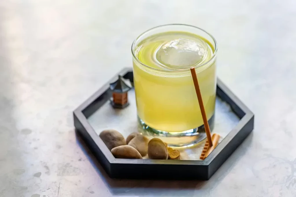 Greenish-yellow drink with ice sphere and stick on a zen garden tray.