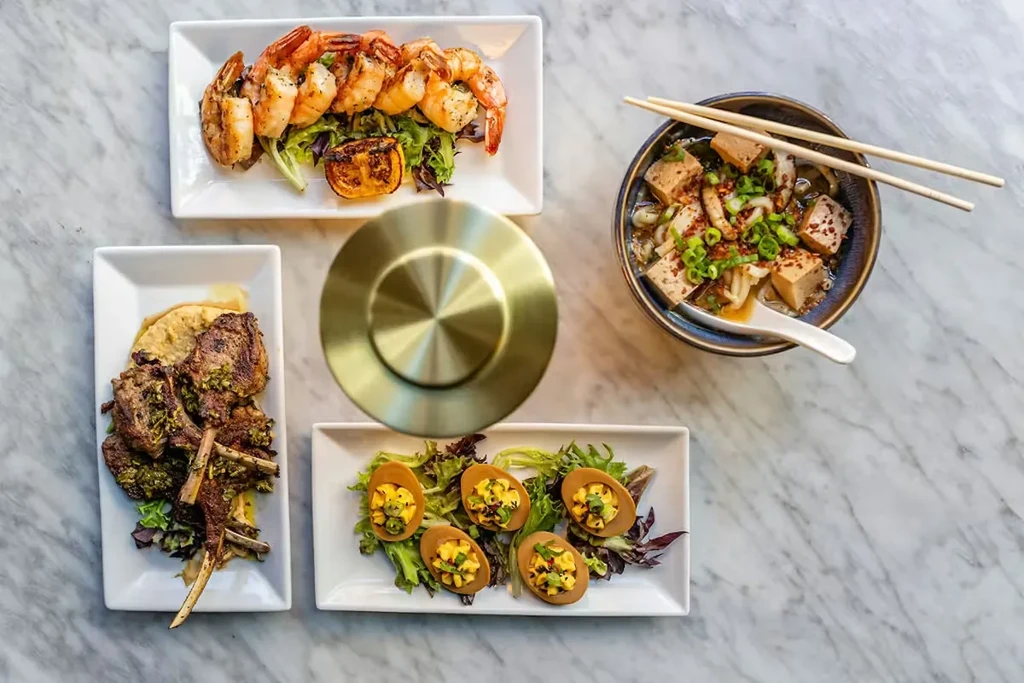 Overhead: grilled shrimp, lamb, deviled eggs, and tofu noodles on marble.