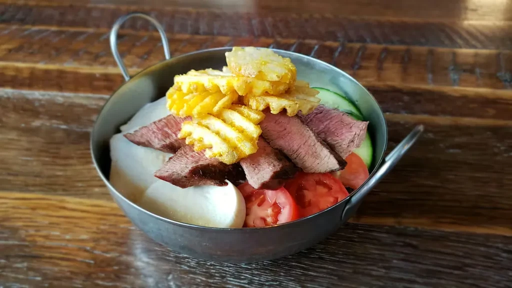 Close-up of medium-rare steak, waffle fries, vegetables in a metal bowl.