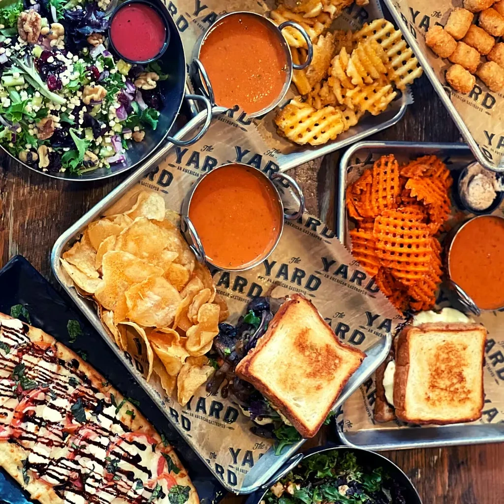 Gastropub table laden with grilled cheese, fries, soup, salad, and flatbread.