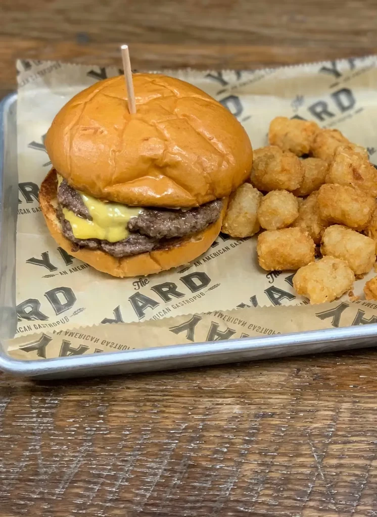 Double cheeseburger and crispy tater tots on a branded metal tray.