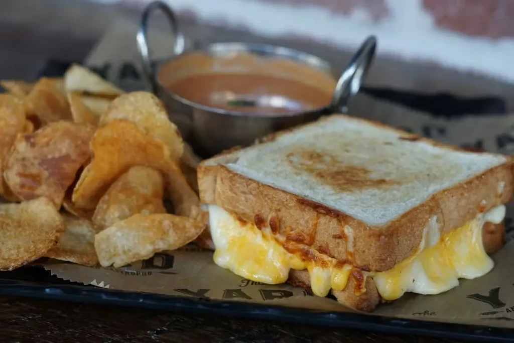 Grilled cheese, potato chips, and tomato soup served on a dark tray.