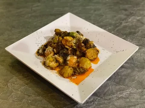 Plated roasted Brussels sprouts with reddish sauce, white dressing, and herbs.