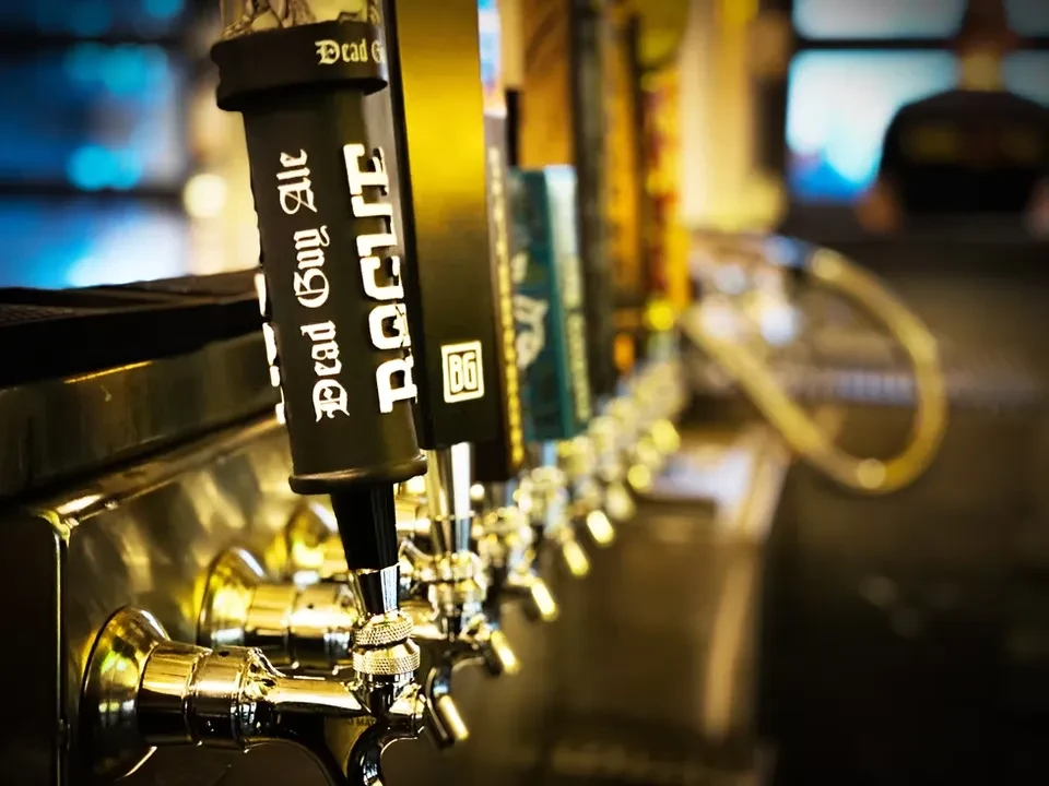 Shiny beer taps, one marked "Dead Guy Ale," with blurred bar background.