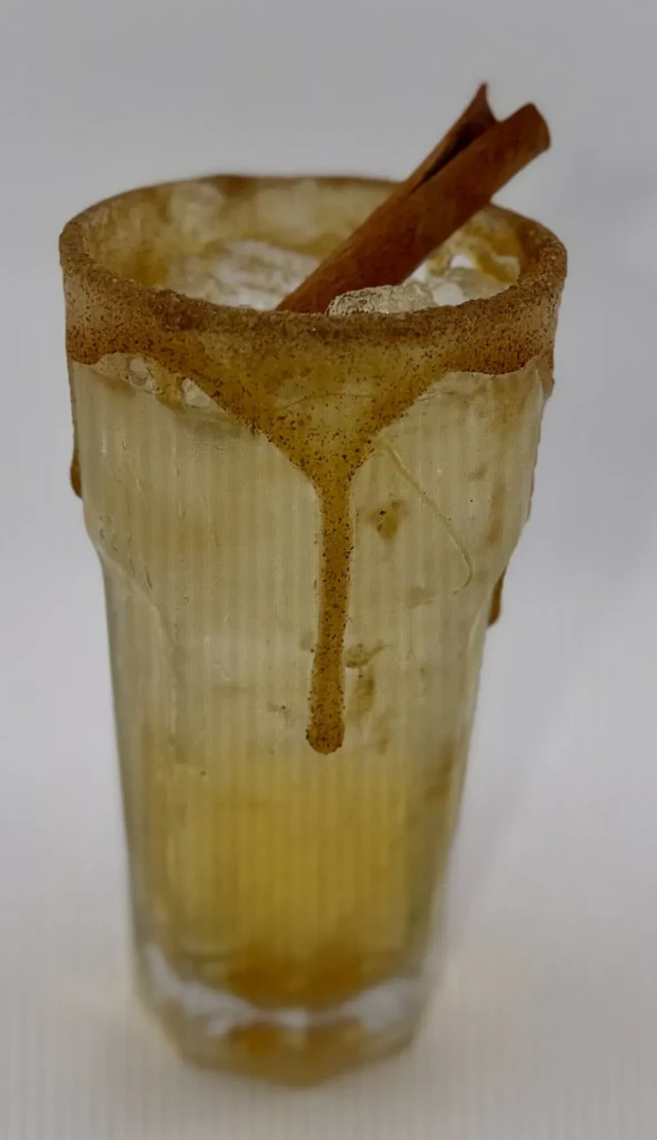 Amber iced drink, cinnamon stick, sugar-rimmed textured glass.