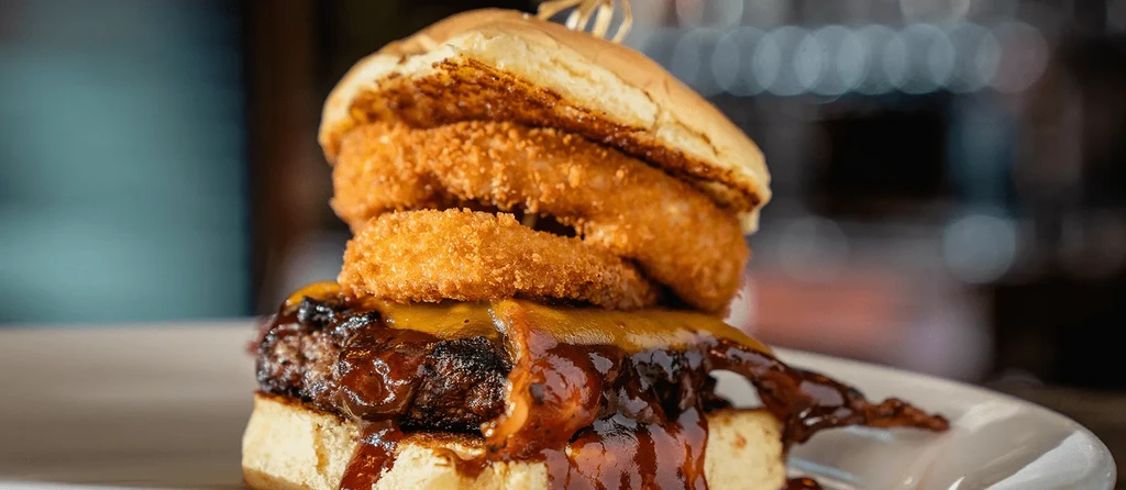 Detailed burger with onion rings, melted cheese, and dripping barbecue sauce.