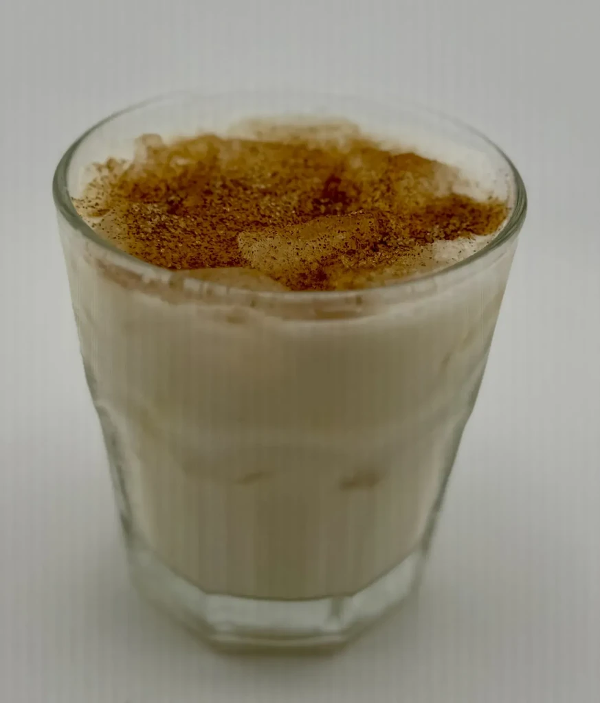 Creamy iced drink in a faceted glass, topped with brown powder.