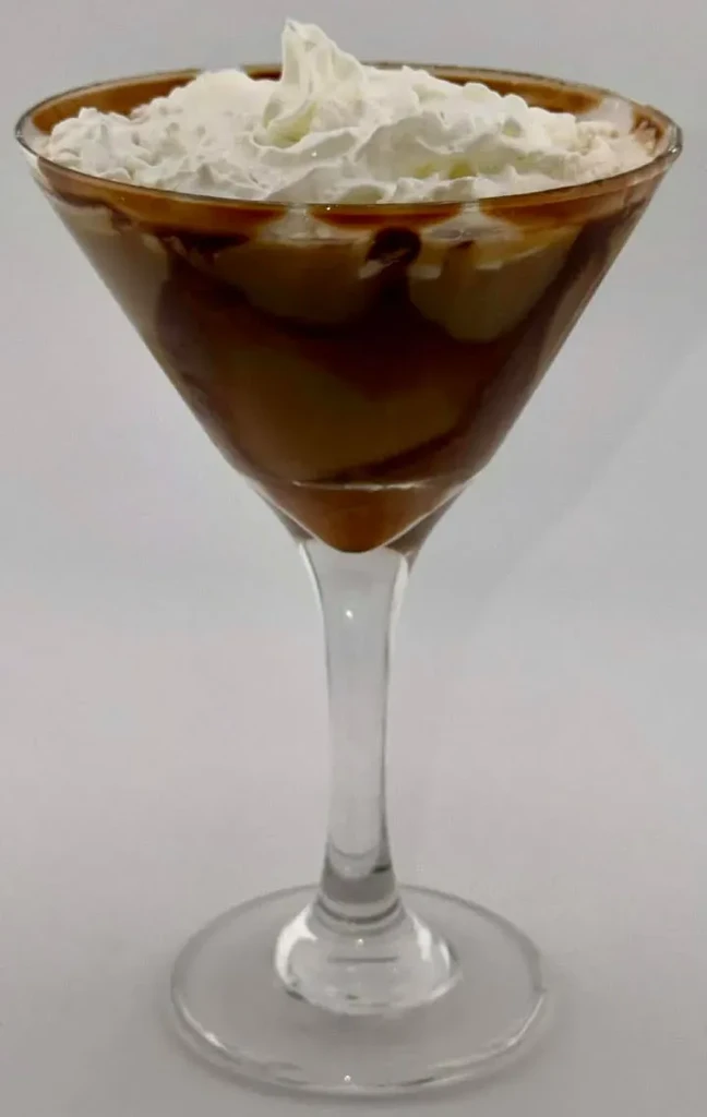 Martini glass with creamy brown drink, chocolate swirls, and whipped cream.