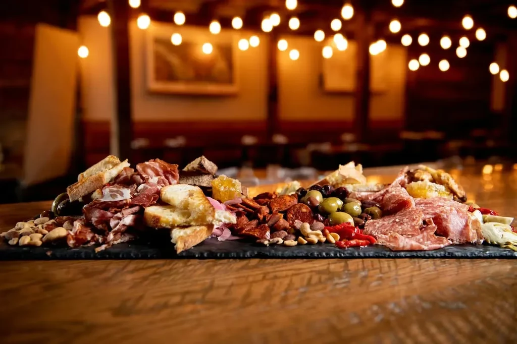Charcuterie board piled with meats, cheeses, bread, olives, nuts, warmly lit.