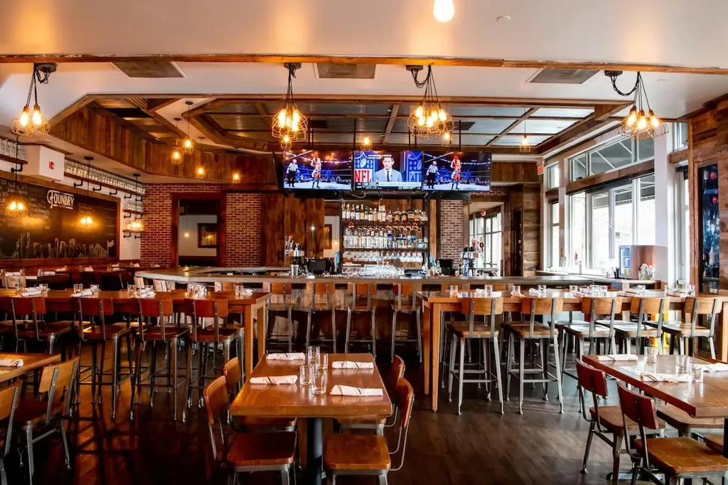 Modern industrial restaurant bar with stocked bar, seating, and TVs.