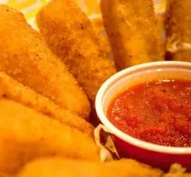 Golden-brown breaded mozzarella sticks in a basket with a side of marinara sauce.