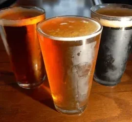 Golden, reddish-amber, and dark beers in glasses on a wooden surface.