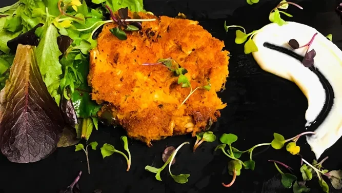 Plated golden-brown patty, fresh salad, sauces, and microgreens.