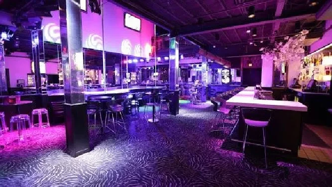 Empty modern bar with purple and pink lighting and mirrored pillars.