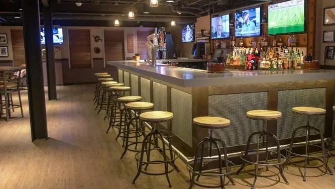 Modern industrial bar counter with liquor bottles, TVs, and metal barstools.