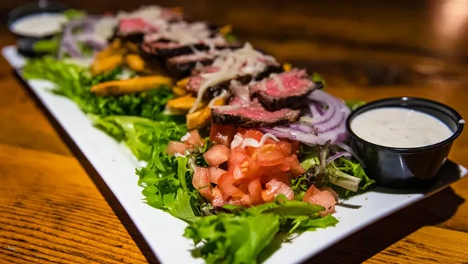 Gourmet steak salad with fries, tomatoes, onion, cheese, and dressings.