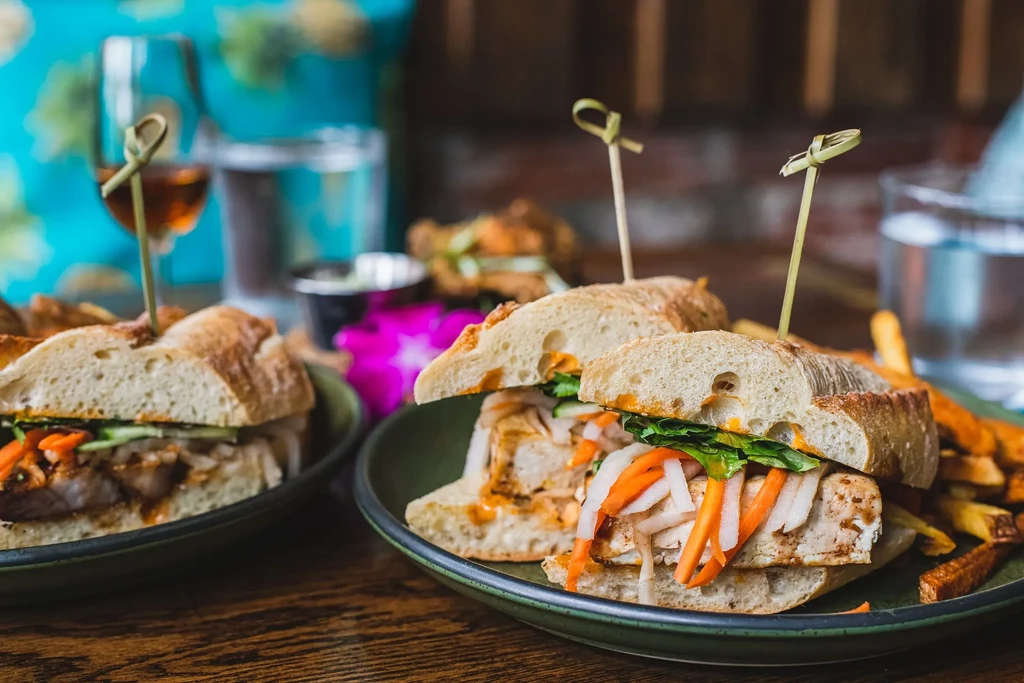 Two banh mi sandwiches filled with grilled protein and vegetables, with fries.