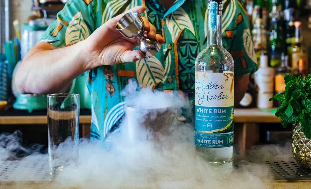 Bartender pours into smoking cocktail shaker, rum and mint nearby.