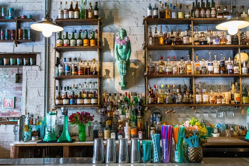 Vibrant bar interior with extensive liquor bottles, mermaid statue, and bar tools.