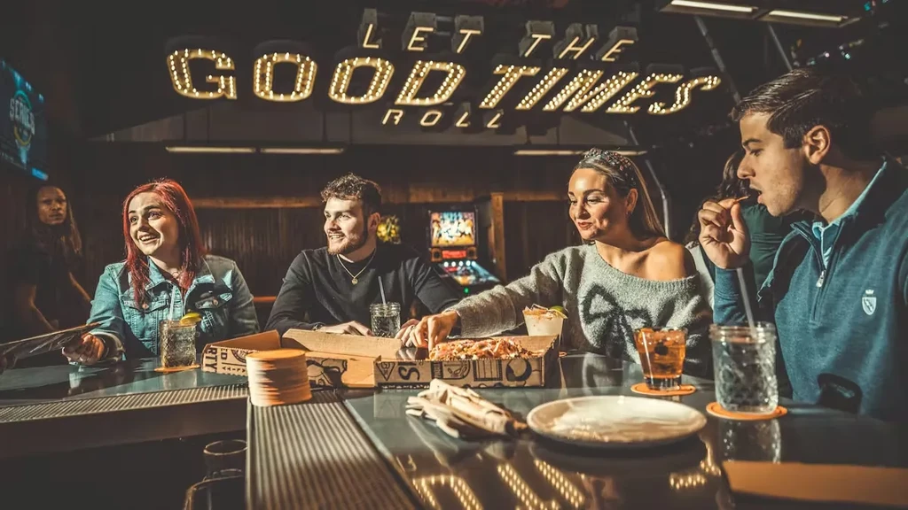 Five people eating pizza and drinking at a casual bar.
