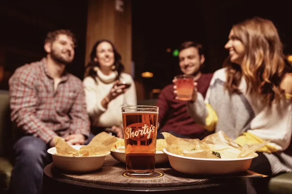 Amber Shorty's beer, fries, and four smiling people at a bar.