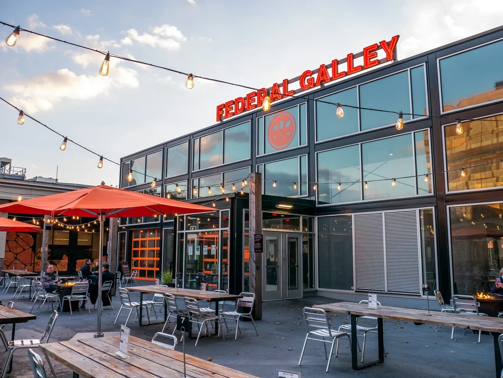 Modern Federal Galley building's patio, with orange umbrellas and patrons.
