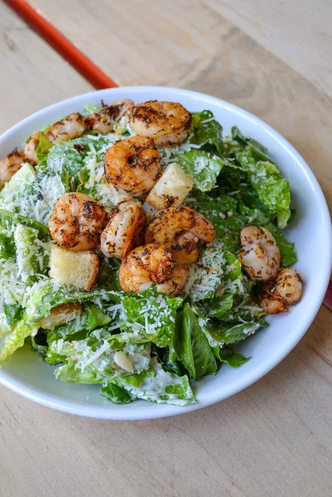 Overhead close-up of a shrimp Caesar salad in a white bowl.