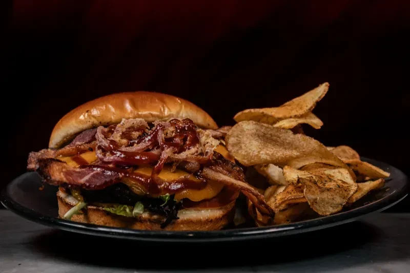A gourmet burger and seasoned potato chips on a black plate.