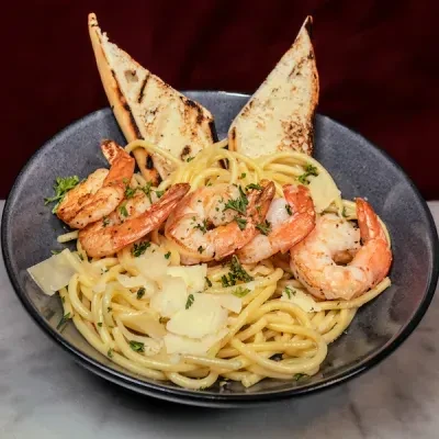 Close-up of shrimp pasta with Parmesan, parsley, and grilled bread.
