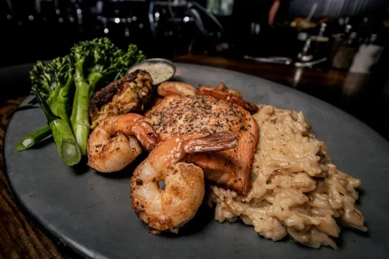 Oval plate with salmon, grilled shrimp, broccolini, pasta, and sauce.