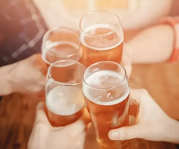 Four hands toast with glasses of amber beer.