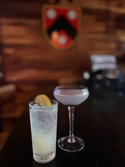 Highball with lemon and lavender coupe cocktails; crest in blurred background.