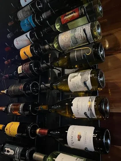 Black metal wine rack filled with numerous wine bottles, labels visible.