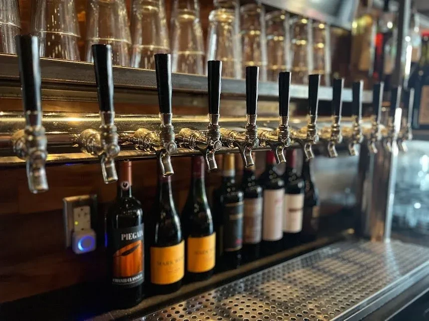 Polished beer taps, wine bottles, and stacked glasses at a bar.