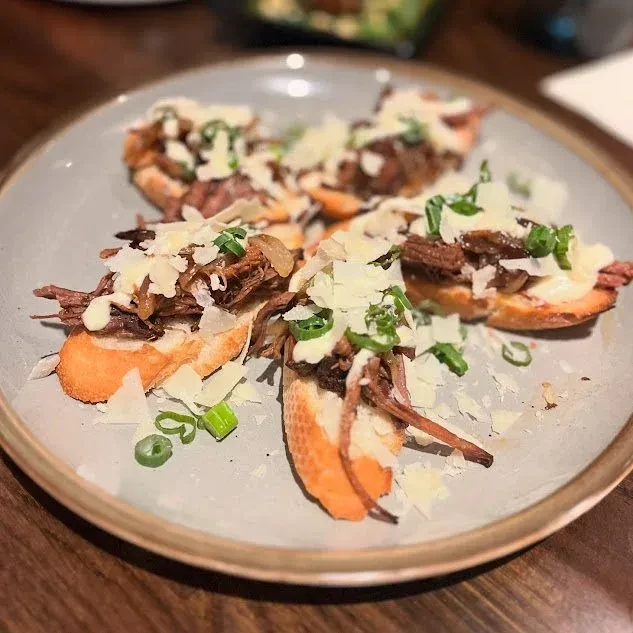 Several bruschetta pieces with shredded meat, white sauce, Parmesan, and green onions.